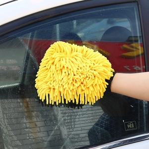 Close-up of yellow chenille microfiber car wash glove wiping wet glass surfaces