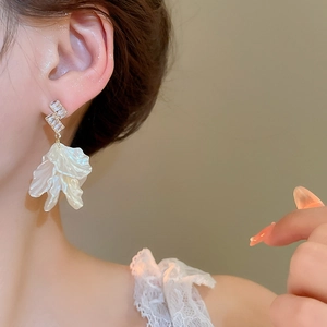 Detail of shell petal tassel earrings with zircons worn by a model on beige background