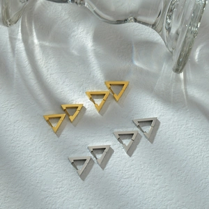 Orecchini a triangolo lucidi color oro e argento su sfondo bianco strutturato con ombre
