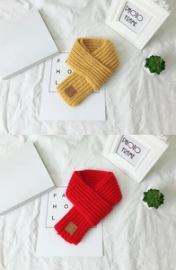 Detail of yellow and red knitted scarves featuring a leather EST LOVE label on white bedding