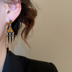 Close-up of vintage golden fringe earrings with amber rhinestones on model's ear