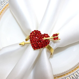 Detail of a gold heart napkin ring with red rhinestones and arrow on a white satin cloth