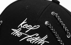 Detail of Keep the Faith embroidery and metal eyelet on black cotton baseball cap