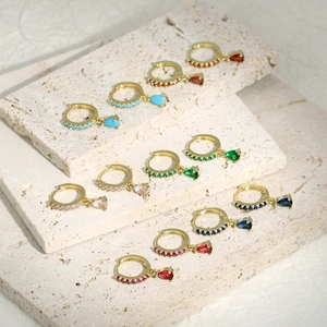 Dettaglio di orecchini con zirconi a goccia colorati su pietra di travertino