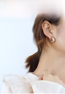 Close-up of elegant polished silver crossover C-shape hoop earrings on a model