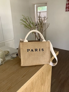 Close-up of woven straw tote bag with long straps and black Paris embroidery on a wooden table