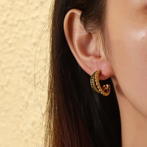 Close-up of gold twist hoop earring with green turquoise stones on female model ear