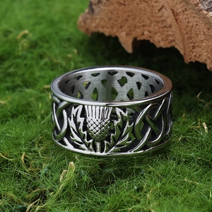 Nahaufnahme eines Edelstahlrings mit Distel- und Keltenknoten-Muster auf grünem Moos
