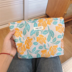 Detail of floral embroidery on a beige makeup bag with orange roses and fabric label