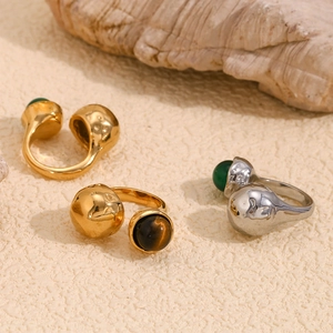 Close-up of gold and silver open rings with green agate stones on a sandy textured background