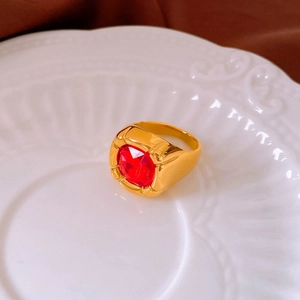 Macro shot of gold-plated ring with a square-cut red stone on a white ceramic plate