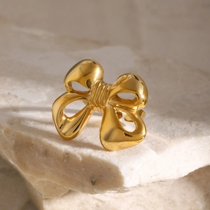 Detailed view of polished 18k gold-plated bow ring on a natural stone textured surface