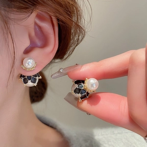 Detail view of gold-plated pearl earrings with black enamel and micro-inlaid rhinestones