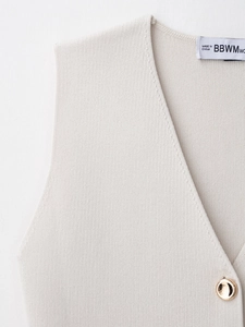 Detailed close-up of beige knit vest featuring elegant golden buttons and fine texture