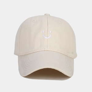 Close-up of cream baseball cap with white embroidered smiley face and cotton twill texture