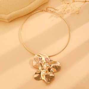 Close-up of a large gold abstract flower pendant on a choker necklace with mirror finish