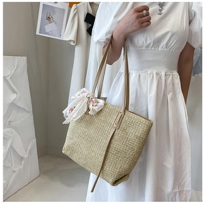 Detail of a large straw tote bag with floral scarf accessory on a shoulder model