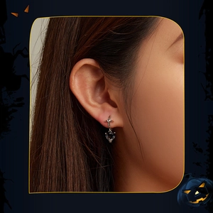 Detail of cross stud earring with heart-shaped dark gemstone pendant on model