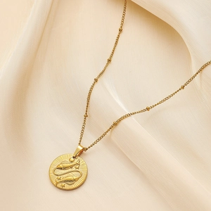 Gold stainless steel necklace with Pisces zodiac coin pendant on soft beige fabric