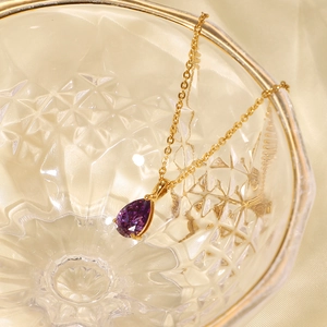 Detail of 18K gold plated teardrop necklace with purple zircon in glass bowl