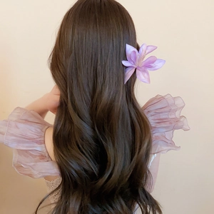 Detail of purple fabric hibiscus hair clip worn on long wavy hair for vacation style