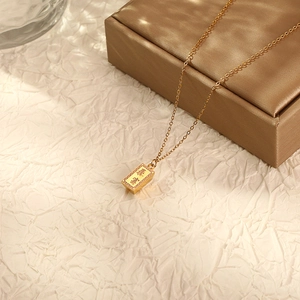Gold brick pendant necklace with Bao Fu Chinese characters on elegant beige background