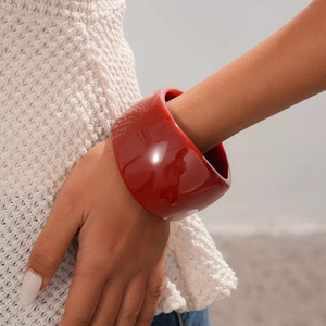 Detail of a retro wide deep red resin bangle worn on wrist with beige knit sweater