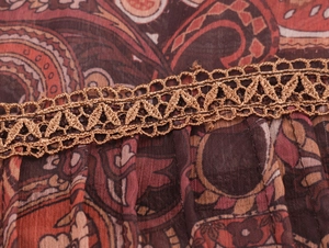 Macro detail of paisley print chiffon fabric with golden crochet lace and pleats