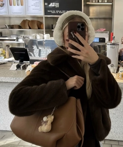 Close-up of a short dark brown faux fur jacket with wide collar and white plush earmuffs