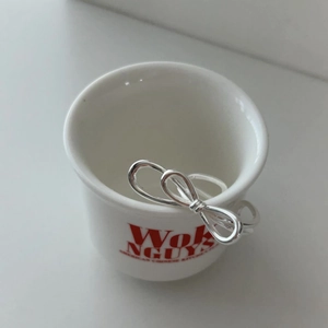 Polished S925 sterling silver bow knot open ring displayed on a white ceramic bowl edge