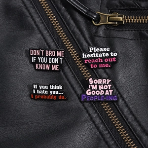 Detail of four colorful enamel pins with sarcastic quotes on a black leather jacket