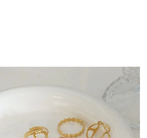 Close-up of gold-plated rings including V-logo design and beaded band on ceramic tray