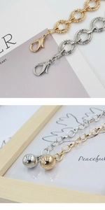 Close-up of metal chain belt with lobster clasp and round ball pendant in gold and silver