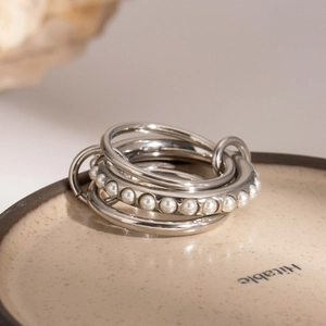 Multi-layer stackable stainless steel ring with white pearls on a ceramic tray