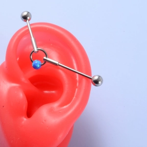 Macro detail of silver industrial barbell earring with blue opal bead on red ear model