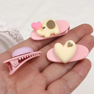 Hand holding cute cartoon elephant and heart hair clips in sweet pink and yellow colors