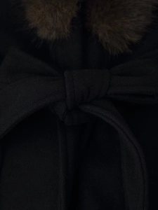 Detail of black wool coat featuring soft brown fur collar and elegant waist bow tie