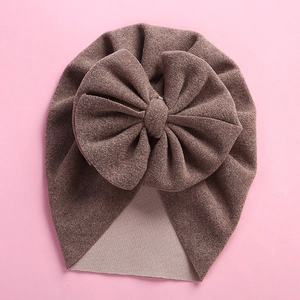 Brown cashmere-like baby beanie with a large decorative bow on a pink background