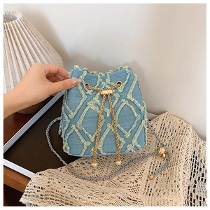 Detail of blue denim bucket bag with diamond embroidery, pearl closure and chain strap