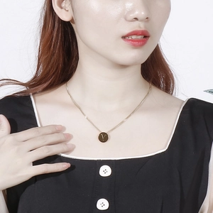 Close-up of gold stainless steel necklace with a round letter V pendant worn by a model