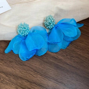 Detailed macro view of bright blue fabric flower earrings with beaded center on wood surface