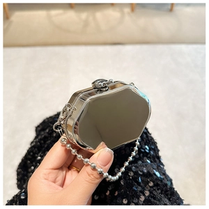 Detail of silver mirror mini hard shell bag with ball chain held in hand for scale