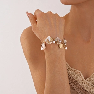 Close-up of ocean-style shell and pearl gold chain bracelet worn on a female wrist