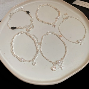 Dettaglio ravvicinato di bracciali argentati con perle d'acqua dolce e ciondoli a cuore