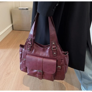 Detail of burgundy PU leather handbag with buckle pocket carried by a model in a black suit