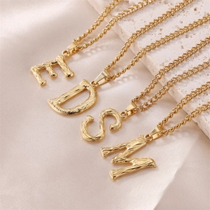Textured gold capital letter necklaces E D S M on elegant silk and stone background