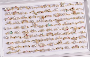 Close-up of golden alloy rings with enamel flowers, pearls and colorful crystals in a box