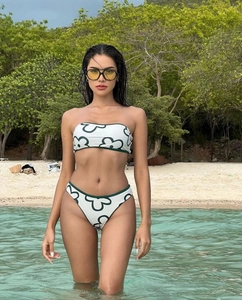 Detail of white bikini with green floral prints featuring strapless top and high cut bottoms