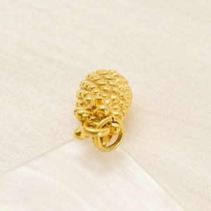 Detailed golden pineapple pendant in stainless steel with textured surface on beige fabric
