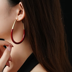 Close-up of a model wearing a gold and red teardrop enamel earring with silver needle